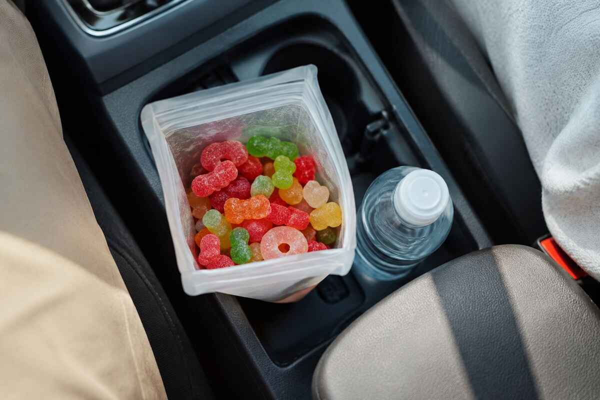 Bag of colorful road trip gummies stored in a car's center console next to a water bottle