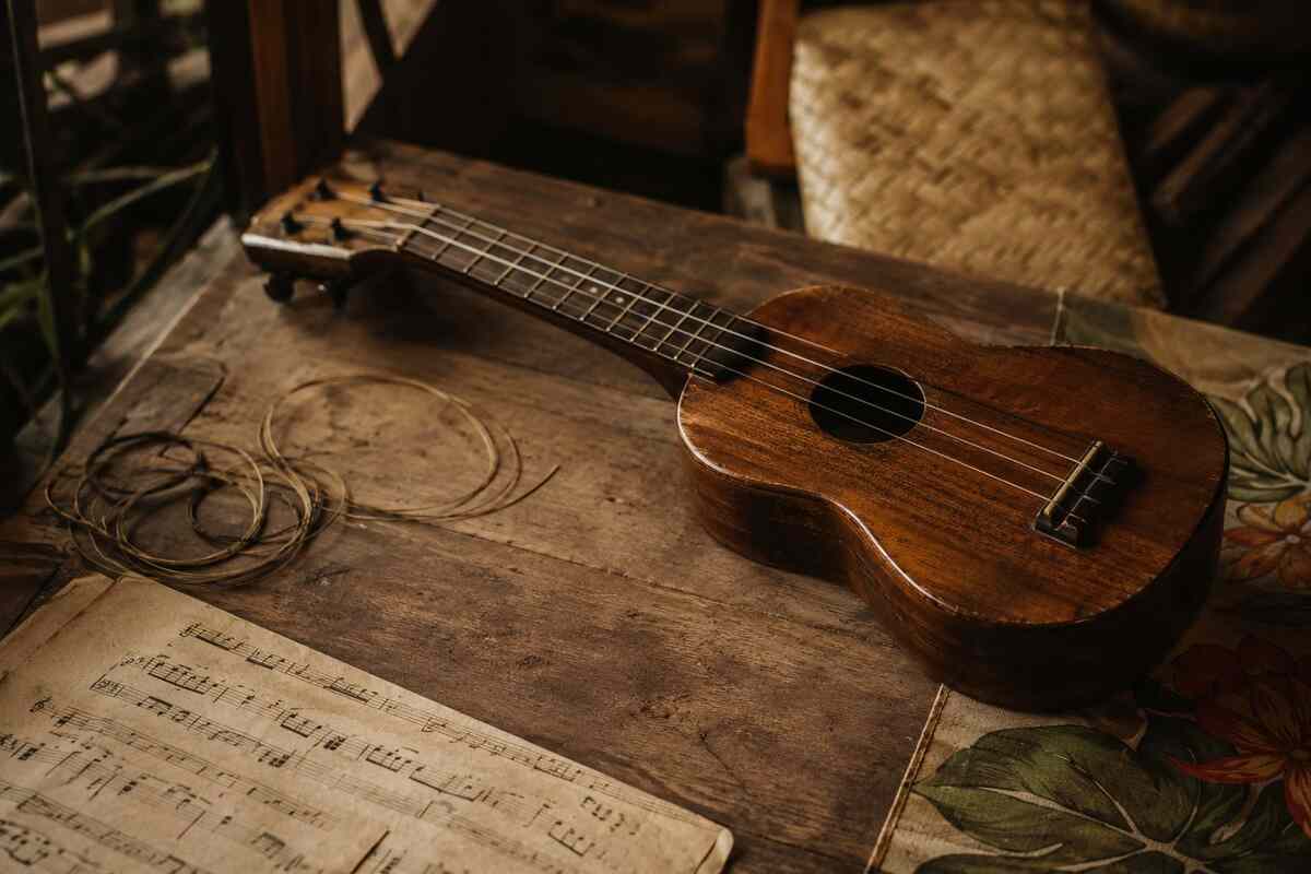 Vintage wooden ukulele with loose strings and old sheet music representing ukulele history